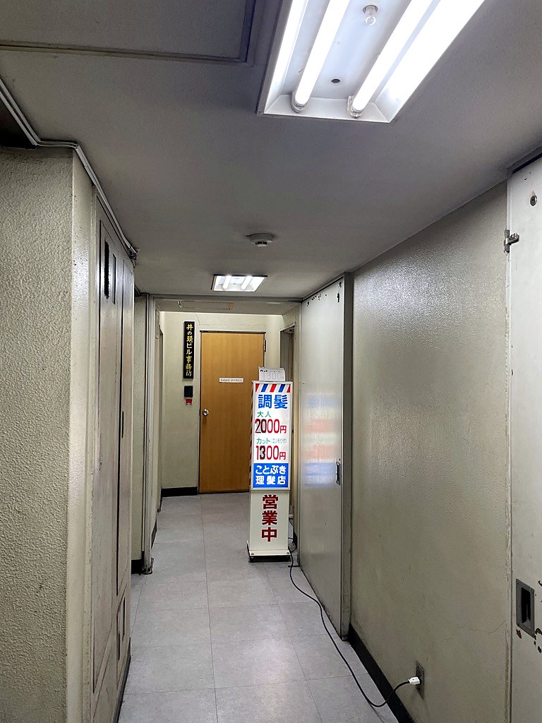 井の頭ビル3階の廊下。奥に、ことぶき理髪店の看板が立っている